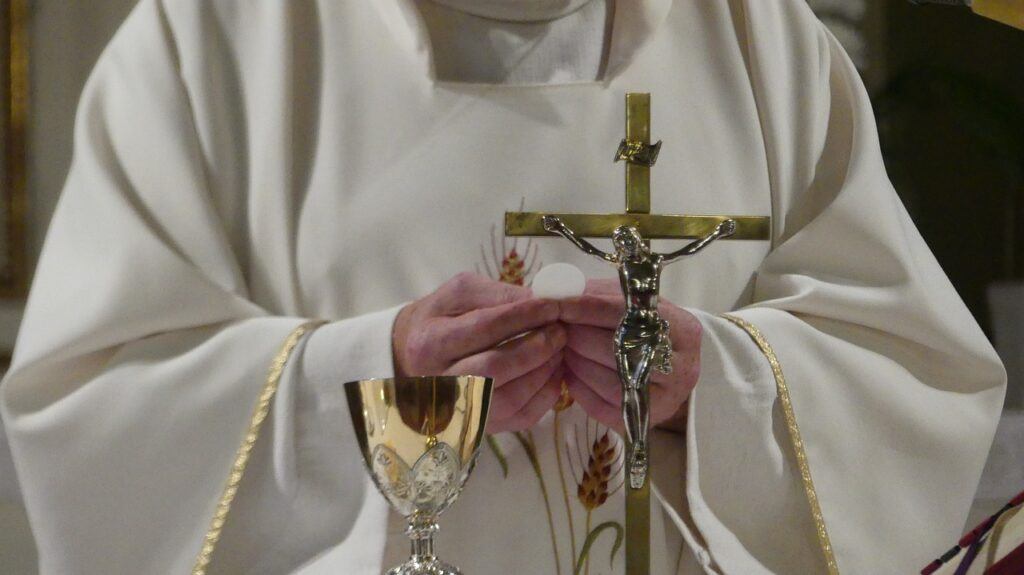 Sacerdote sosteniendo una hostia y un crucifijo durante la celebración de la Eucaristía.