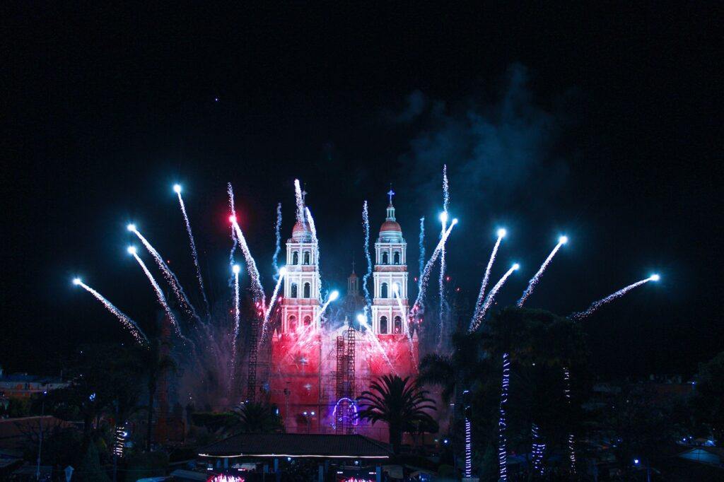 Fuegos artificiales iluminando el cielo nocturno, con una iglesia de dos torres en el fondo, representando las festividades católicas.