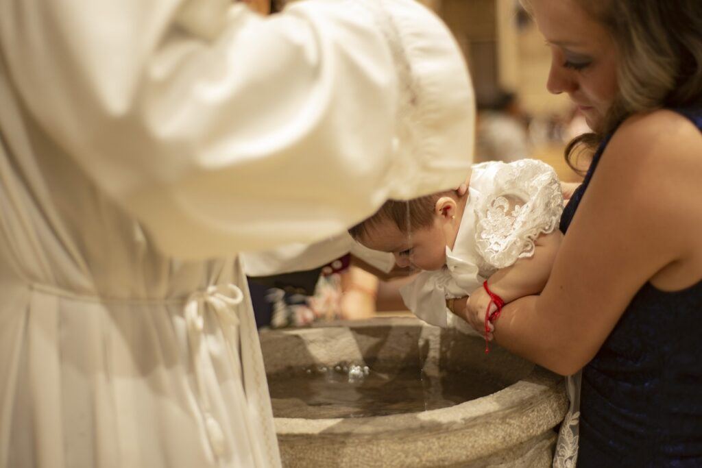 Un sacerdote bautizando a un bebé en una pila bautismal, sostenido por su madre, durante el sacramento del Bautismo.