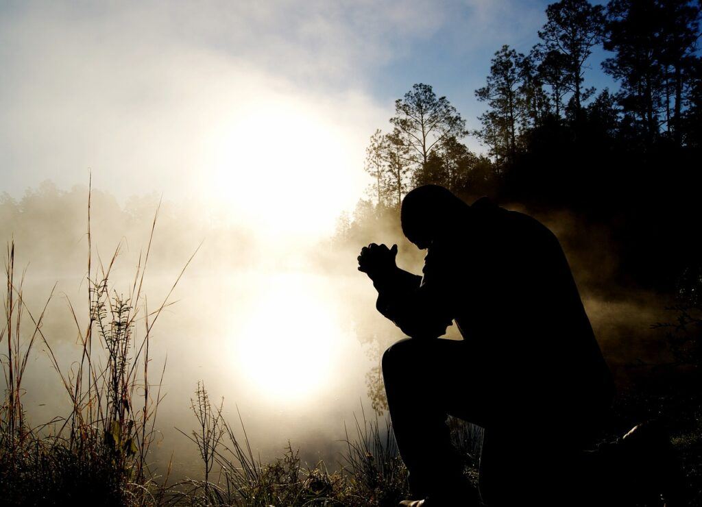 Hombre orando al amanecer junto a un lago